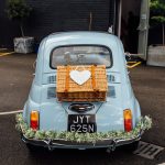 Fiat 500 wedding car decorated with bumper garland and picnic basket